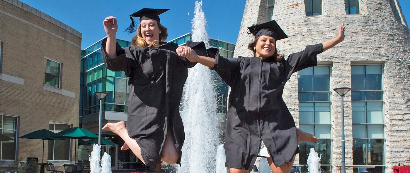 two graduates jumping in front of the University Center fountain